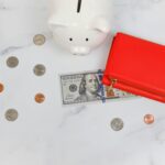 Overhead view of piggy bank, red wallet, and US dollars on marble surface.